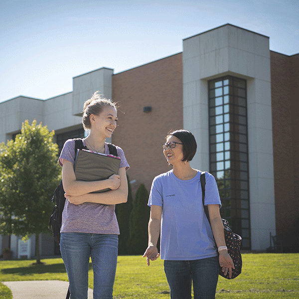 Two female students standing and laughing in front of the Jasper Classroom Building